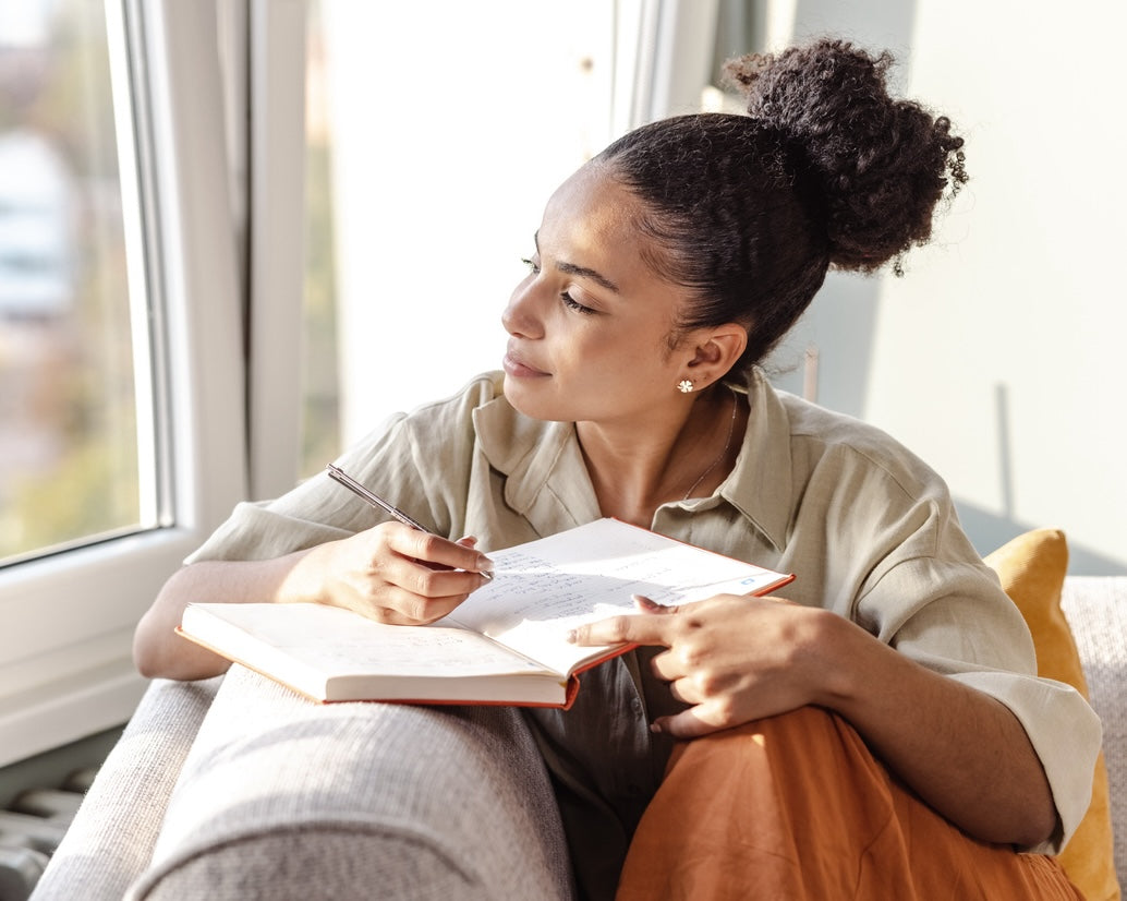 A young woman is at home, she is sitting on the sofa in the living room and writing notes.